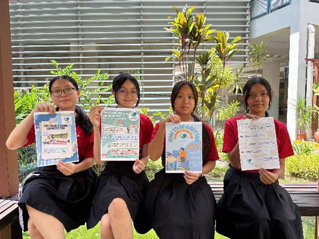 A group photo of 4 Zhenghua Secondary School students posing with e-posters designed by them.